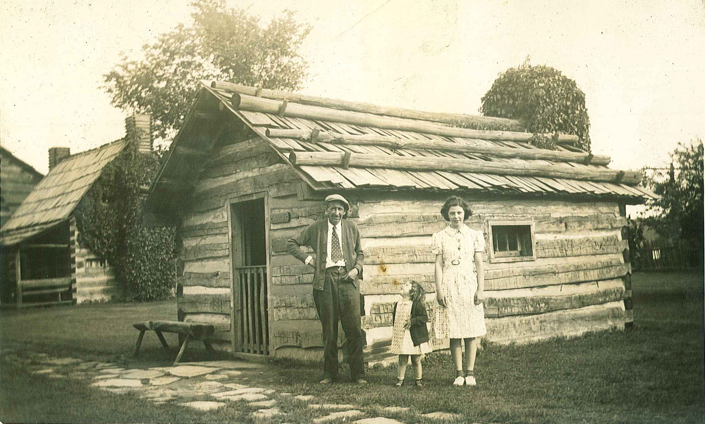 Ben with children Martha and Ruth standing in front of cabin at Schoenbrunn Village, circa 1940.